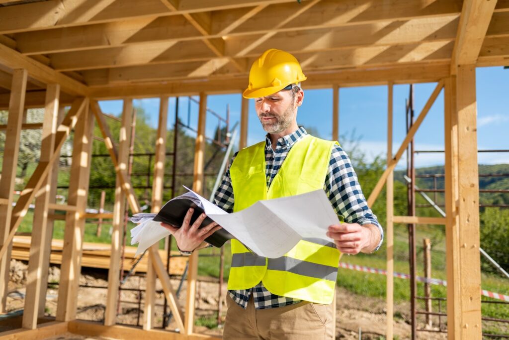Contractor reviewing blueprints on-site with safety helmet and plans.